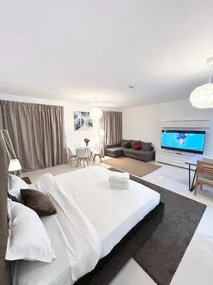 a white bedroom with a large bed and a flat screen tv at Seaside Spacious Studio with Vibrant Vibes in JBR By SWEET HOMES in Dubai