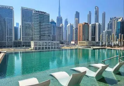 a swimming pool with white chairs and a city skyline at HAVN - Studio Unit in 15 Northside, Business Bay in Dubai