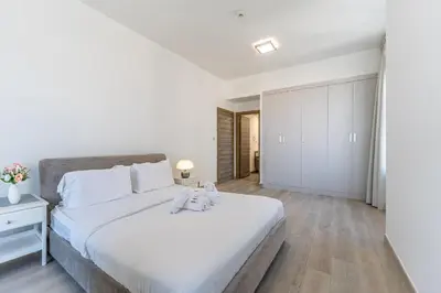 a white bedroom with a large white bed and wooden floors at HAVN - 2 Bedroom Apartment in Bloom Tower, JVC in Dubai