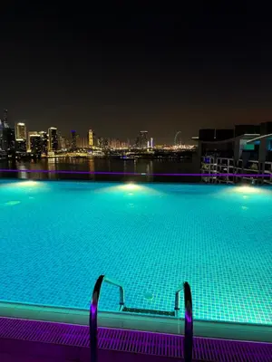 a large swimming pool with a city skyline at night at Beachside Bliss: Stylish New Studio at Seven Palm in Dubai