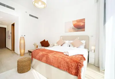 a white bedroom with a large bed with an orange blanket at EasyGo - Azizi Riviera 15 Community View in Dubai