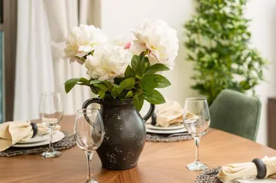 a black vase with white flowers on a table with glasses at Prime Retreats @ Burj Crown by Emaar, Downtown dubai in Dubai