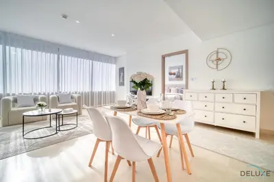a white dining room with a table and chairs at Special Offer Stylish 1BR with Scenic Views & Pool by Deluxe Holiday Homes in Dubai