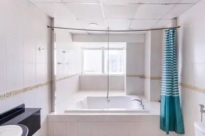 a white bathroom with a tub and a window at Ensuite Rooms in CoLiving Apartments in Marina in Dubai