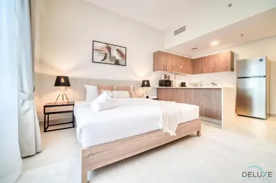 a bedroom with a large white bed and a kitchen at Stylish Studio Apartment at Casa Grande, JVC by Deluxe Holiday Homes in Dubai