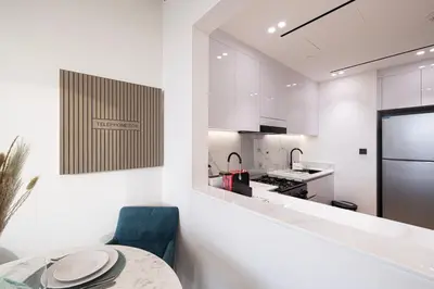 a white kitchen with a table and a blue chair at Spacious Balcony, 1BR, Pool, Full Kitchen at JVC in Dubai
