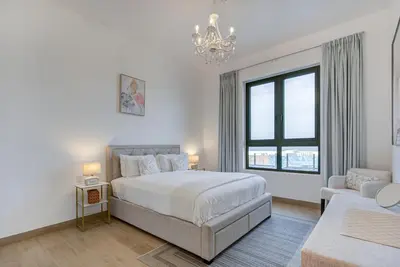 a white bedroom with a bed and a chandelier at Trophy - Serene Abode near the Coast in Dubai