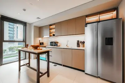 a kitchen with a stainless steel refrigerator and a table at Stayis l 2BR Iconic Burj Khalifa View Partial in Dubai