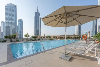 a pool with an umbrella and a chair next to a building at Stayis l 2BR Iconic Burj Khalifa View Partial in Dubai