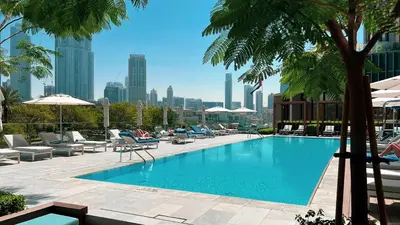 a swimming pool with chairs and palm trees and a city at SmartStay at Address Opera - Unique Burj Khalifa Views - Brand New Luxury Residences in Dubai