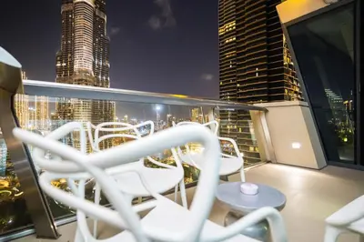 a balcony with chairs and a city skyline at night at Vacay Lettings - Stunning Burj Khalifa fountain view near Dubai mall in Dubai
