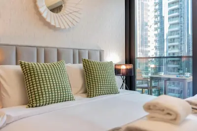 a bedroom with a white bed with green pillows and a window at Amazing 2BR Burj Kalifa View in Dubai