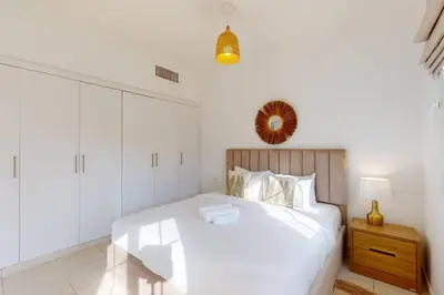 a white bedroom with a white bed and a wooden cabinet at The Springs - Tranquil Two Bedroom Villa in Dubai