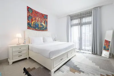 a white bedroom with a bed and a large window at Old Town Luxury: 1-BR Apartment with Large Terrace & Burj Khalifa View in Dubai