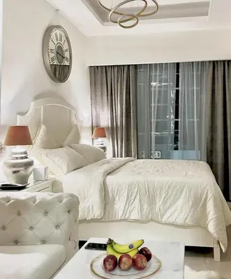 a white bedroom with a bed and a table with a plate of fruit at Dubai Galaxy in Azizi Riviera Luxury Studio in Dubai