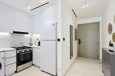 a white kitchen with a refrigerator and a stove at Chic 1BR in JVC with Balcony, Near Mall & Parks in Dubai