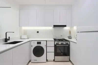 a white kitchen with a stove and a dishwasher at Chic 1BR in JVC with Balcony, Near Mall & Parks in Dubai