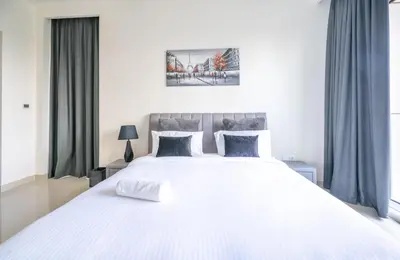 a bedroom with a large white bed with blue curtains at Homes Beyond l Spacious 2BR Creekside Lifestyle in Dubai