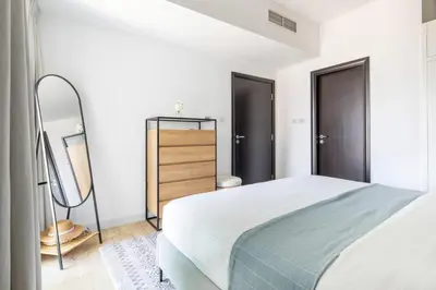 a white bedroom with a bed and a mirror at Frank Porter - La Riviera Tower in Dubai