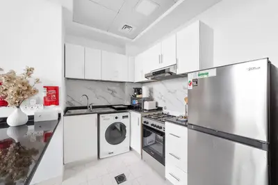 a white kitchen with a refrigerator and a dishwasher at Silkhaus Luxury Studio Near Silicon Shopping Mall in Dubai