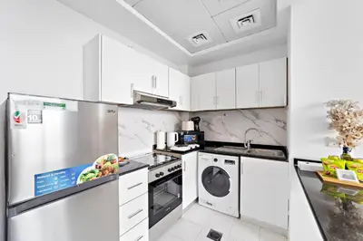 a white kitchen with white cabinets and a dishwasher at Modern Luxurious Studio in Dubai Silicon Oasis in Dubai