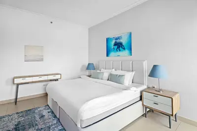 a white bedroom with a large bed and a table at Downtown 3BR Sleeps 9 Balcony, Full Kitchen, Near Metro in Dubai