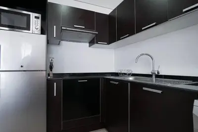 a kitchen with black cabinets and a stainless steel refrigerator at Cozy Studio in Sports City in Dubai