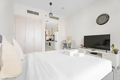 a white bedroom with a large bed and a tv at Comfortable Studio in Damac Hills in Dubai