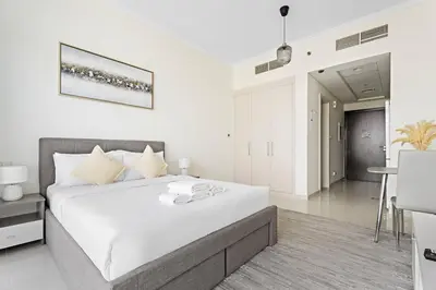 a white bedroom with a large bed and a table at Cozy Studio in Damac Hills in Dubai