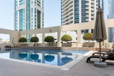a swimming pool with an umbrella and some buildings at Stylish 1BR Apartment with City View Balcony Pool and Parking in Dubai
