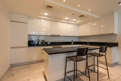 a kitchen with white cabinets and two bar stools at Noora Tower I Habtoor City I Spacious 3BDR plus maid room I Business Bay in Dubai