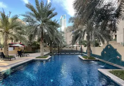 a swimming pool with palm trees in a courtyard at Stylish 1BR in Old Dubai Balcony, Smart TV, Full Kitchen in Dubai