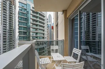a balcony with white chairs and tables and buildings at Comfortable 1BR Apartment in Marina Tower, Dubai Marina by Deluxe Holiday Homes in Dubai