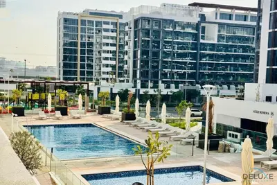 a hotel pool with chairs and buildings in the background at Comfy 1BR in Azizi Riviera 8, Al Merkadh by Deluxe Holiday Homes in Dubai