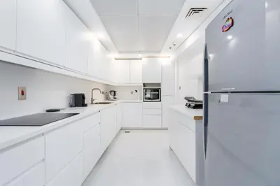 a white kitchen with white cabinets and a refrigerator at High class apartment in Dubai