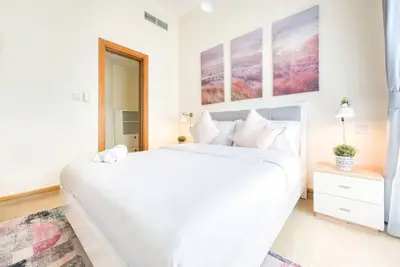 a white bedroom with a large white bed and a mirror at Exclusive 2BR Apartment in Madison Residency - Close to Dubai Internet City Metro Station in Dubai