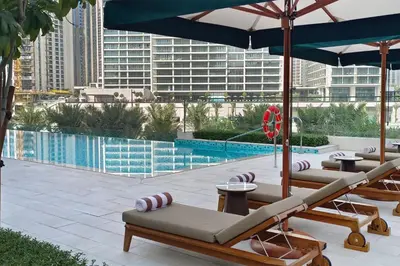 a group of lounge chairs and umbrellas next to a pool at Spacious 1-Bedroom in Summer, Lagoon Access Feature - Allsopp&Allsopp in Dubai