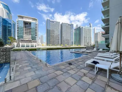 a pool with chairs and umbrellas in a city at 1 Bedroom Business Bay Bliss with a Canal View in Dubai