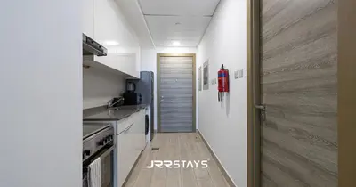 a kitchen with white walls and a wooden floor at Sophisticated Studio JVC - Breathtaking City View in Dubai