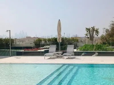 two chairs and an umbrella next to a swimming pool at Studio Apartment in Vincitore Palacio Arjan in Dubai