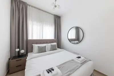 a white bedroom with a bed and a mirror at Comfortable 2BD apartment next to metro & mall in Dubai