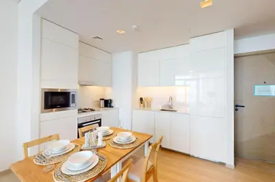 a kitchen with white cabinets and a wooden table with chairs at Palace Residences - Modern One Bedroom in Dubai