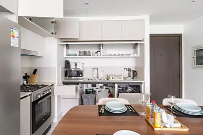 a kitchen with white cabinets and a wooden table at Silkhaus Skyline View | Exclusive Neighbourhood in Dubai