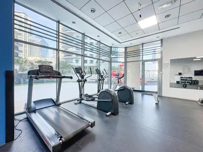 a gym with treadmills and ellipticals in a room with windows at Trophy - Magical Marina 1BDR connected to Metro Station in Dubai