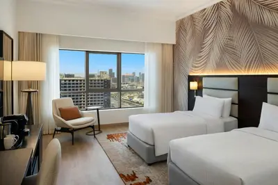 a hotel room with two beds and a chair and a window at Marriott Hotel Production City, Dubai in Dubai