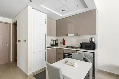 a kitchen with a white table and a stove top oven at Beautiful 1 BR with Gym, Pool & Kid's Playground in Dubai