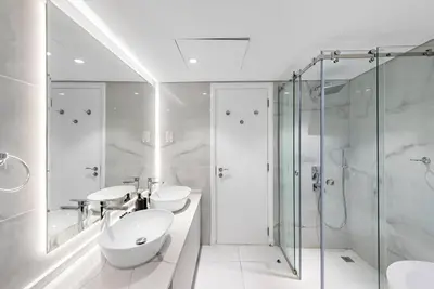 a white bathroom with two sinks and a shower at First Class 1BR Modern & Stylish Living in Dubai
