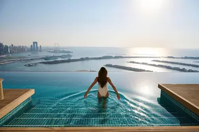 a woman sitting in a infinity pool looking out at the city at Palm Tower Luxury 1BR Sea View Suites with 5 Star Hotel Amenities in Dubai