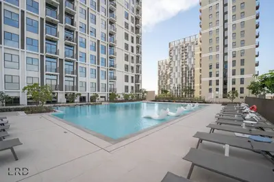 an outdoor swimming pool with chairs and buildings at New Cozy 1BR Dubai Hills in Dubai