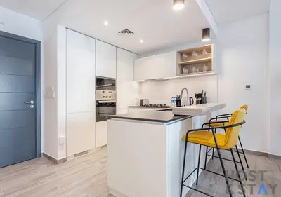 a kitchen with white cabinets and yellow bar stools at 1BR Belgravia Apartment with pool view in Dubai